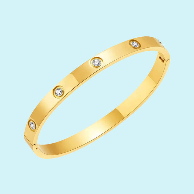 A sleek gold bracelet with a smooth finish, featuring evenly spaced round diamond accents. The bracelet is set against a light blue background, highlighting its elegant and luxurious design.
