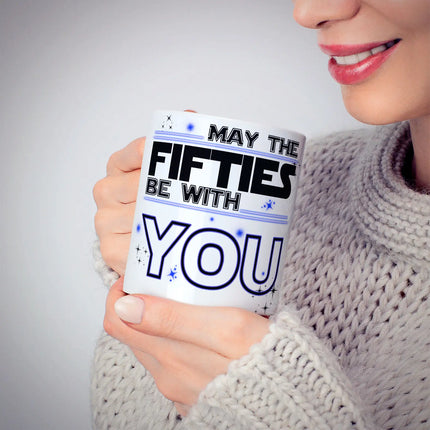Women sipping from a White ceramic mug with "MAY THE FIFTIES BE WITH YOU" in black and bluetypography, decorated with stars - perfect 50th birthday gift
