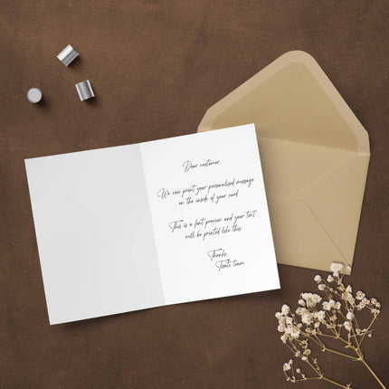 Open blank greeting card with elegant script text, beige envelope, and dried flowers on brown surface.