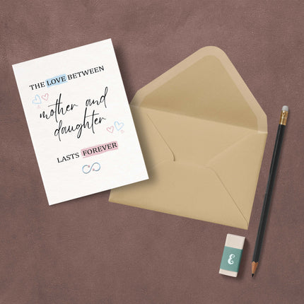 Mother and daughter greeting card with beige envelope, pencil, and eraser on a brown surface