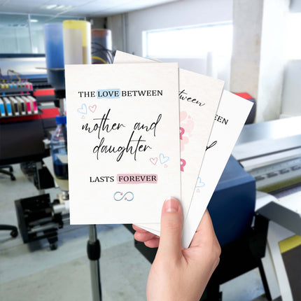 Hand holding personalised mother and daughter greeting cards in front of a printing machine