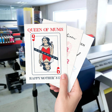 Hand holding the Queen of Mums Mother's Day Card inside a professional printing studio.