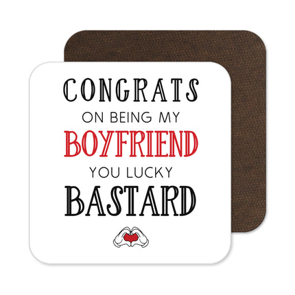 Square drink coaster with rounded corners and a visible cork backing. The white surface features the humorous text CONGRATS ON BEING MY BOYFRIEND YOU LUCKY BASTARD