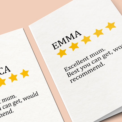A close-up, angled shot of two white greeting cards. Both feature a personalized "review" design. One card displays the name "EMMA" above five yellow stars and the message "Excellent mum. Best you can get, would recommend."