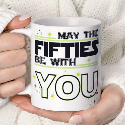 Novelty coffee mug featuring 'MAY THE FIFTIES BE WITH YOU' slogan in black and yellow style typography with decorative stars on white ceramic background, perfect 50th birthday gift