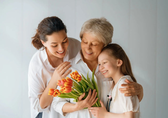Woman holding flowers with two children against a plain background