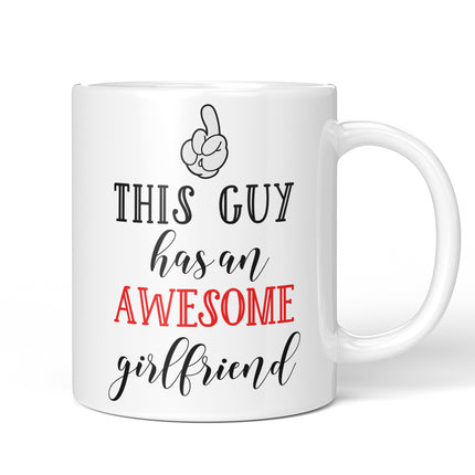 A close-up of a hand holding a white coffee mug that features the text "This Guy Has An Awesome Girlfriend" in black and red script, with a cartoon thumb pointing toward the person holding the cup.